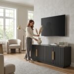 Woman arranging decor on a custom dark grey fluted TV stand with gold handles in a modern living room. Wholesale furniture manufactured by MMK Furniture Makers.
