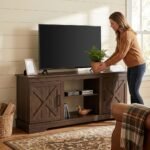 Woman organizing decor on a custom dark walnut barn door TV stand with no back panel in a bright living room. High-quality OEM/ODM living room furniture supplied by MMK TRADE INC.