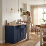 Woman preparing coffee at a navy blue kitchen island storage cabinet with wood countertop in sunny dining room