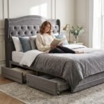 A woman relaxing on a comfortable grey velvet tufted storage bed in a bright bedroom, showcasing custom premium furniture manufacturing by MMK TRADE INC.