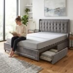 Young woman reading on a modern grey velvet upholstered bed with under-bed storage drawers, manufactured by MMK Furniture Makers.