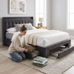 A woman organizing clothes in the pull-out storage drawer of a dark tufted velvet bed frame, manufactured by MMK Furniture Makers for USA wholesale market.