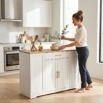 A woman organizing a modern white wooden trolley with a light wood top and gold handles in a bright kitchen setting, manufactured by MMK Furniture Makers.