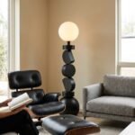 The-stacked-geometric-floor-lamp-standing-next-to-a-low-profile-modern-lounge-chair-in-a-well-lit-living-space-illustrating-its-full-floor-to-ceiling-presence-and-architectural-impact.
