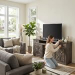 Woman styling a dark wood farmhouse entertainment center with X-brace cabinet doors in a bright living room by MMK TRADE INC.
