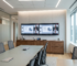 A sleek solid walnut commercial AV credenza sitting beneath a large dual-screen video conferencing setup in a modern corporate boardroom.