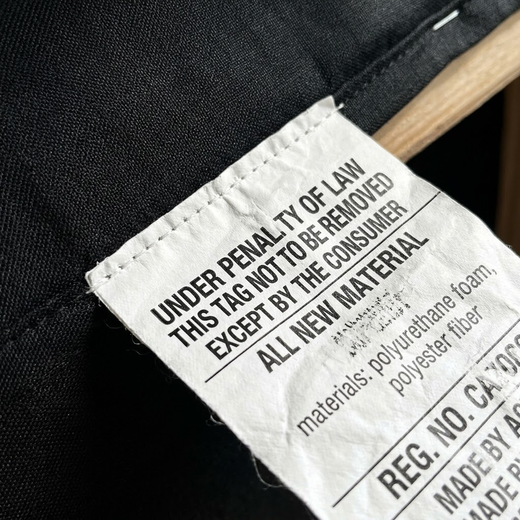 Close up of a mandatory US Uniform Law Label stitched into the bottom decking of a wholesale commercial sofa, stating compliance with California TB 117-2013.